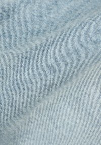Gros plan d'un tissu en denim bleu clair montrant un tissage diagonal détaillé et une texture avec des variations subtiles de couleur.