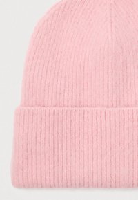 Berretto lavorato a maglia rosa chiaro con risvolto, che mostra una texture morbida e pelosa su uno sfondo bianco.