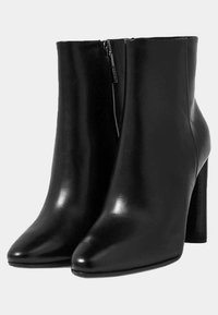 Bottines en cuir noir avec une finition brillante, bout pointu et un talon haut en bloc. Prévue d'une fermeture éclair latérale pour un enfilage facile.