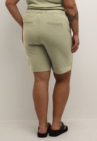 Shorts de color verde claro, hasta la rodilla, hechos de una tela suave con un corte relajado. Cuentan con una cinturilla elástica y dos bolsillos en la parte trasera.