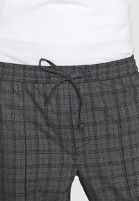 Grå rutiga joggers med elastisk midja och justerbar dragsko, med en texturerad tyg och vertikala linjer.