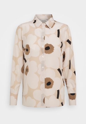 Chemise beige à manches longues boutonnée, grand imprimé floral blanc et marron, col pointu.