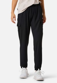 Black cargo pants with an elastic waistband, tapered fit, and two side pockets. Paired with white athletic shoes. Smooth fabric texture.