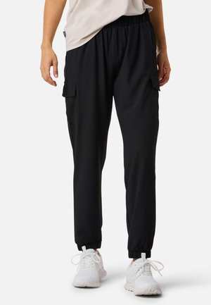 Black cargo pants with an elastic waistband, tapered fit, and two side pockets. Paired with white athletic shoes. Smooth fabric texture.