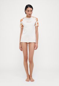 Short-sleeve white rash guard with orange floral pattern on sleeves and collar, featuring a Ripcurl logo on the front. Smooth fabric texture.