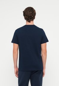 Tricou din bumbac de culoare bleu marin, cu mâneci scurte, decolteu rotund și croială dreaptă. Textură netedă; design minim, fără logo-uri sau modele vizibile.