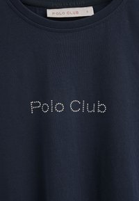 Camiseta azul marino hecha de una tela suave con "Polo Club" en piedras brillantes en el pecho. Cuello redondo, manga corta. Talla S.