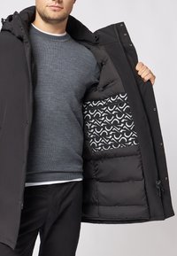 Czarna kurtka puchowa z kapturem, z zapięciem na zamek błyskawiczny w wewnętrznej kieszeni oraz podszewką w geometryczny wzór w białym i czarnym kolorze.