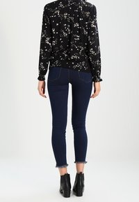 Blusa nera a fiori con maniche lunghe, abbinata a jeans skinny blu scuro con orli sfilacciati e stivali neri alla caviglia.