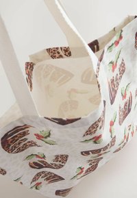 Plátěná taška s bílým podkladem, zdobená leopardím vzorem a cesmínou. Zpevněné krémové uchy; jemná textura a prostorný interiér.