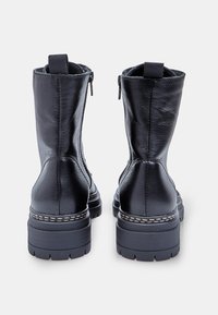 Botine din piele neagră, cu încărcare cu fermoar, vârf rotund și finisaj texturat. Prezintă o talpă groasă cu detalii de cusătură decorative.