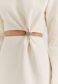 Robe en tissu blanc présentant un détail noué à la taille, rehaussée d'une boucle en strass argenté pour plus de raffinement.