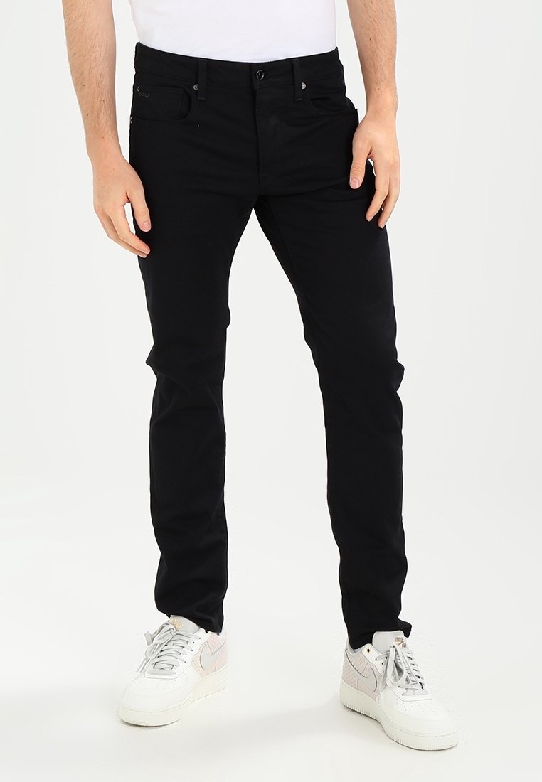 Jeans slim fit negros de algodón, con cierre de cremallera y botón, cinco bolsillos y detalles de costura sutiles.