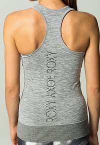 Mujer que lleva una camiseta de deporte sin mangas gris con "ROXY" impreso verticalmente en la parte posterior, mostrando los omóplatos y la parte superior de la espalda.