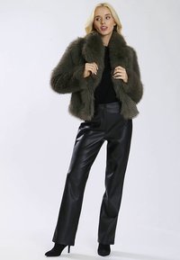 Kurtka z imitacji futra w oliwkowej zieleni z szerokim kołnierzem, zestawiona z czarnymi skórzanymi spodniami i czarnymi szpilkami. Gładka faktura i nowoczesny design.