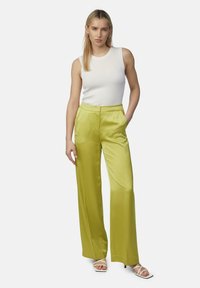 Satynowe spodnie o szerokich nogawkach w jaskrawym limonkowym kolorze, zestawione z dopasowanym białym topem na ramiączkach i białymi, eleganckimi szpilkami. Gładka tekstura, czyste linie.