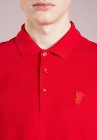 Polo rouge en mélange de coton, avec un col classique, une fermeture à trois boutons et un logo texturé brodé sur la poitrine gauche.