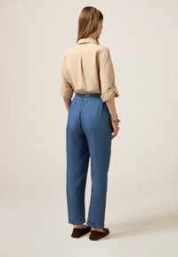 Beige skjorta med uppvikta ärmar, tillsammans med blå denimbyxor med elastisk midja och bruna låga skor.