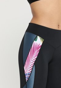 Svarta leggings med en sidopanel i blått med ett mönster av rosa och gröna palmblad, framhävt med svarta sömmar.