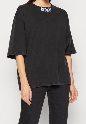 T-shirt nera oversize in cotone con collo rotondo, maniche corte e logo del brand bianco a contrasto sul colletto. Tessuto semplice.