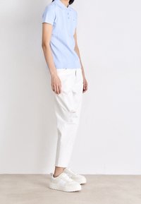 Polo azzurro chiaro con maniche corte, tre bottoni, abbinato a jeans bianchi strappati e sneakers bianche chunky.