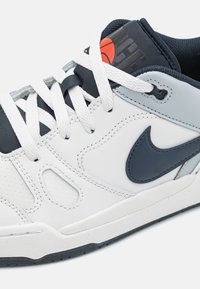 Sneakers bianchi con superiore in pelle perforata, dettagli in blu navy, lacci bianchi piatti e una patch con il logo sulla linguetta. Suola testurizzata per una migliore aderenza.