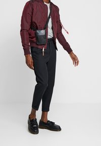 Burgundi bomberi takki, harmaa t-paita, mustat lyhyet housut ja mustat nahkaiset loaferit tupsuilla. Mukana on pieni musta olkalaukku.