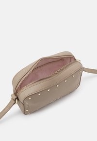 Borsa a tracolla rettangolare beige con borchie dorate, doppie cerniere e una morbida fodera interna rosa. Presenta una tracolla per un facile trasporto.