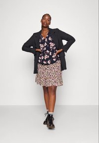 Black blazer over a floral blouse with pink and white flowers, paired with a layered floral skirt in pink and beige tones, and black boots.