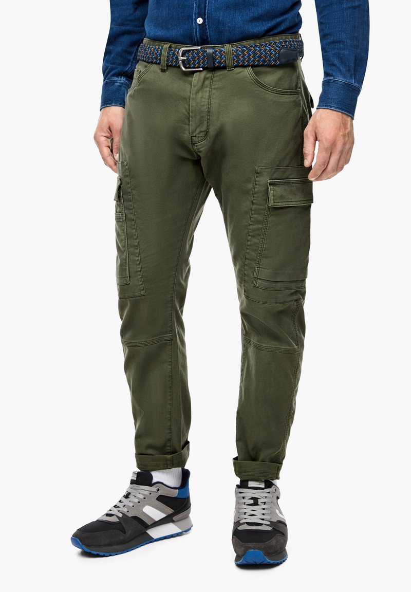 Mann trägt olivgrüne Cargohosen mit Seitentaschen, einen gewebten Gürtel, ein blaues Jeanshemd, weiße Socken und schwarze und graue Turnschuhe.