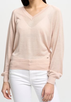 Maglione a maniche lunghe rosa chiaro con scollo a V e orlo a costine. Presenta polsini arricciati e una trama sottile. Indossato sopra jeans bianchi.