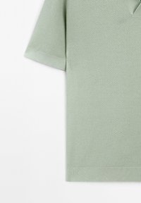 Polo shirt verde menta a maniche corte con tessuto testurizzato, caratterizzato da un collo a V e polsini a costine. Design semplice con una finitura pulita.