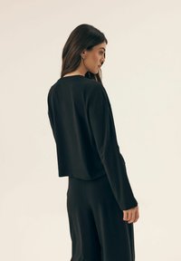 Czarny krótki top z długim rękawem, wykonany z miękkiego materiału, o luźnym kroju, z nieco oversize'owymi rękawami i okrągłym dekoltem.