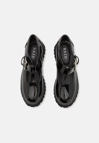 Sapatos de verniz pretos com um design de tiras em T, fivela ajustável e sola robusta. O interior apresenta o logótipo da marca. Textura suave.