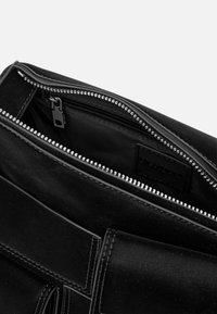 Czarna skórzana torebka na zamek, charakteryzująca się gładką teksturą i eleganckim designem. Wnętrze ma minimalistyczne czarne wykończenie.