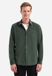Groene, langarmige button-up shirt van gestructureerde stof, met een borstzak en contrasterende knopen, gedragen over een wit T-shirt.