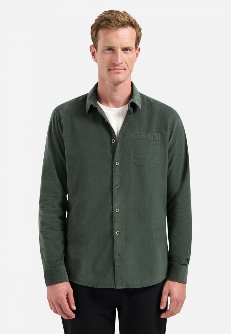 Groene, langarmige button-up shirt van gestructureerde stof, met een borstzak en contrasterende knopen, gedragen over een wit T-shirt.