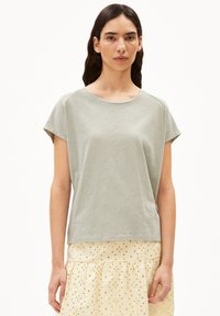 Lichtgroen T-shirt met korte mouwen en ronde hals. Zacht, lichtgewicht materiaal met een ontspannen pasvorm. Gepaard met een gestructureerde gele rok.