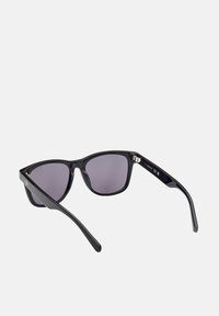 Gafas de sol de plástico negro con montura angular, lentes ahumados grises y brazos laterales rectos. Cuenta con un acento plateado en la bisagra.