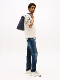 Chaleco de punto gris claro sobre una camiseta verde, jeans azules y zapatillas grises. Bolsa azul oscura colgada del hombro, modelo de lado.