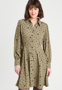 Robe à boutons olive avec de longues manches bouffantes, motif floral noir, corsage ajusté et jupe évasée. Texture de tissu lisse.