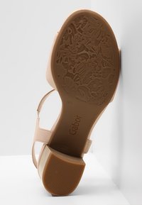 Sandale beige pour femme montrant une semelle à motif floral détaillé, un talon bloc avec une prise texturée et une bride à la cheville, taille 4½.
