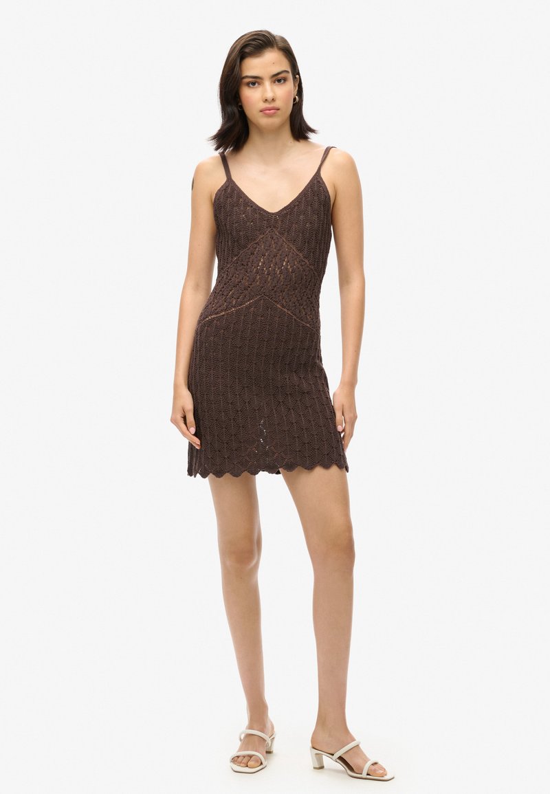 Robe tricotée marron avec un décolleté en V, des bretelles fines, un ourlet festonné et une silhouette cintrée, mettant en valeur des motifs texturés tout au long.