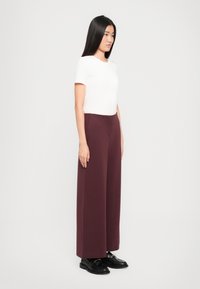T-shirt blanc à manches courtes associé à un pantalon large bordeaux. Les pantalons présentent une texture lisse et une taille propre. Des chaussures noires complètent le look.