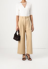 Vitt åtsittande topp med V-ringning och genomskinlig panel, i kombination med vida beige byxor, svarta klackar med remmar och en liten svart handväska.