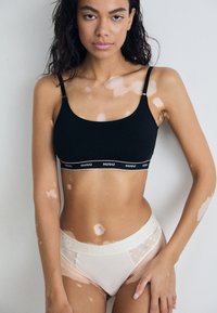 Bralette en coton noir avec bretelles réglables et bande élastique présentant un logo blanc. Sous-vêtements beige avec des accents en tulle à pois et une ceinture de logo.