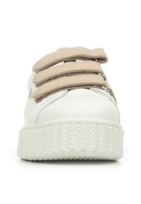 Witte sneaker met een dikke, gestructureerde zool en drie beige klittenbandsluitingen bovenop, bekeken van de voorkant.