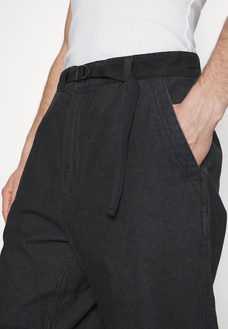 Svarta byxor med ett tygbälte, sidofickor och en avslappnad passform. Materialet har en mjuk textur med subtila sömmar.