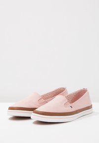 Zapatillas sin cordones de lona rosa claro con suela de goma marrón, entresuela blanca y interior estampado. Presentan cortes laterales y detalle con el logo de la marca.