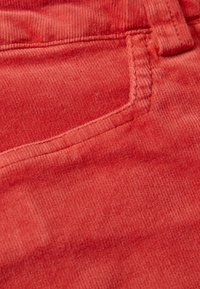 Röd kordflorsduk med vertikala ribbor, som har en sydd fickdetalj och synlig textur. Närbild som visar material och färg.